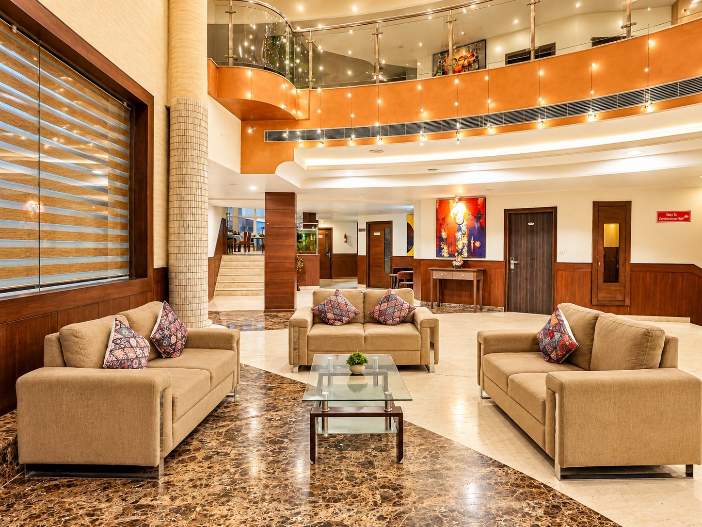 Un vestíbulo de hotel con una zona de estar central, una escalera y un letrero para salón de conferencias.