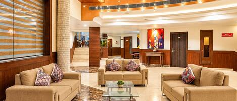 Un vestíbulo de hotel con una zona de estar central, una escalera y un letrero para salón de conferencias.