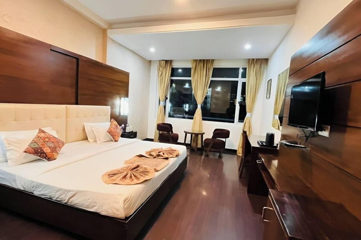 A hotel room with a large bed, a TV, a desk, and a chair.