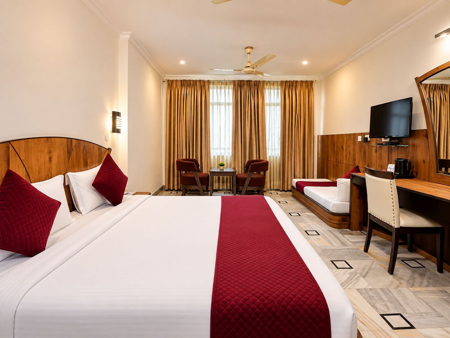 Quarto de hotel com cama grande, escrivaninha, cadeira, televisão e ventoinha no teto.