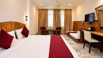 A hotel room with a large bed, a desk, a chair, a television, and a ceiling fan.