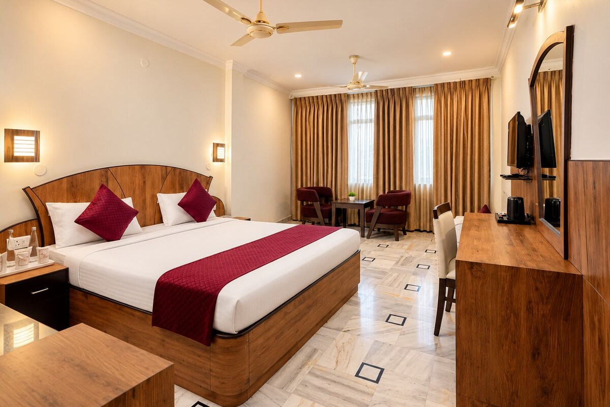 A hotel room with a large bed, a desk, two chairs, a television, and a ceiling fan.