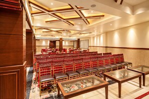 A conference room with rows of red chairs, a glass table, and wooden paneling on the ceiling. - The Altruist Katra Hotel (Katra)