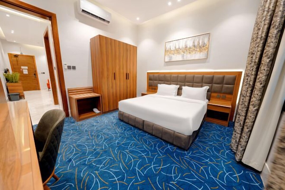 Een hotelkamer met een groot bed, een houten garderobe, een bureau en een blauw kamerkleed.