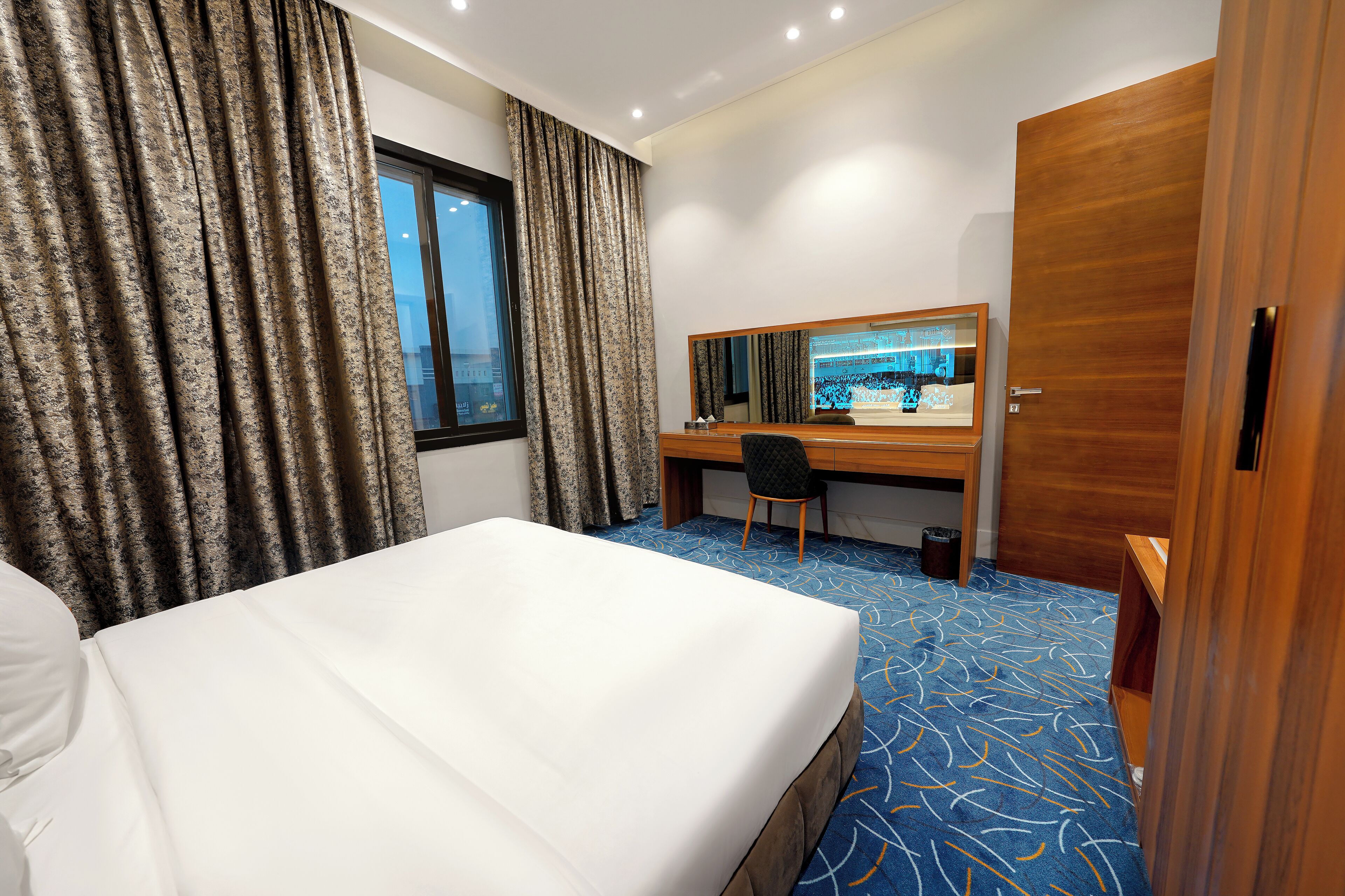 A hotel room with a bed, a desk, a chair, and a large mirror.