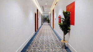 A hotel hallway with patterned carpet, wooden doors, and a red emergency exit sign.