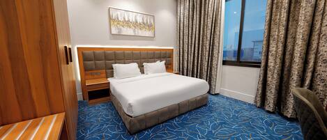 A hotel room with a large bed, a wooden wardrobe, a nightstand, and a window with curtains.