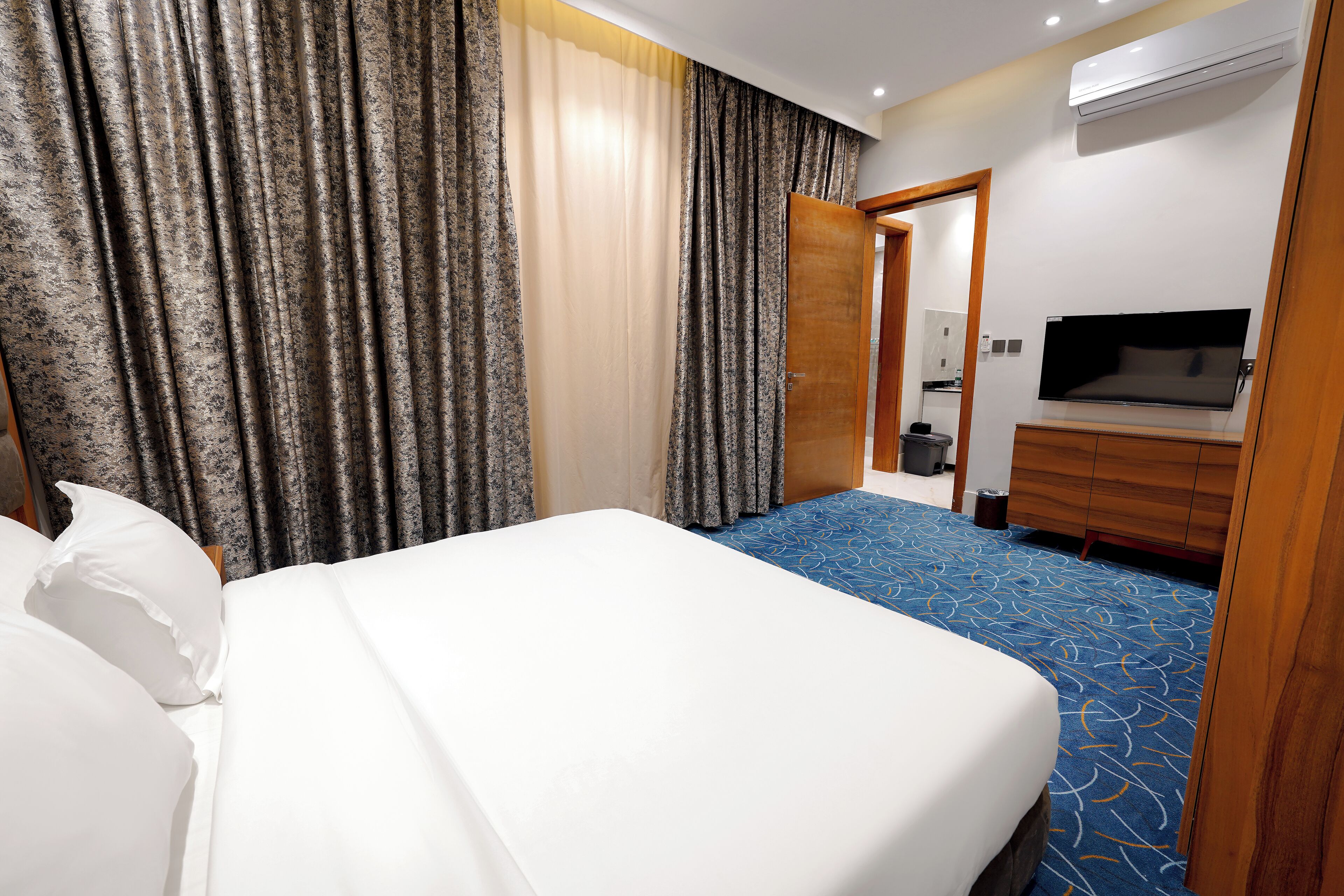A hotel room with a bed, curtains, a TV, a dresser, and a carpet.