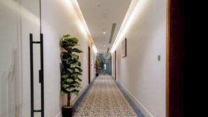 A hallway with patterned carpet, potted plants, and a staircase in the distance.