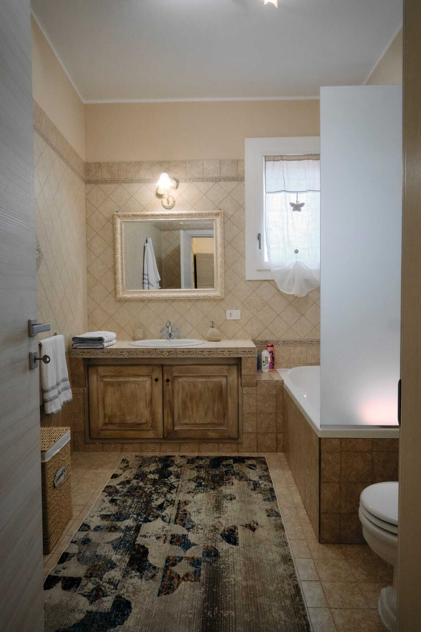 A bathroom with a sink, mirror, and toilet. There is a patterned rug on the floor.