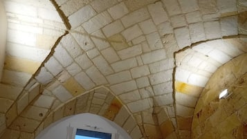 Een kamer met een gewelfd plafond van stenen tegels, een witte muur en een klein raam met een digitaal scherm.