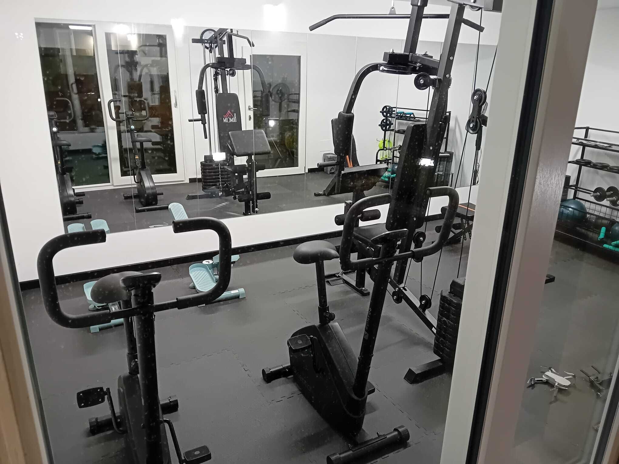 Een fitnessruimte met diverse trainingsapparaten, een spiegelwand en een rek voor gewichten.