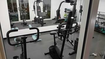 Een fitnessruimte met diverse trainingsapparaten, een spiegelwand en een rek voor gewichten.