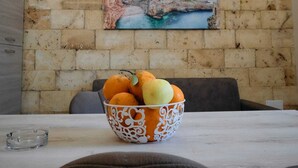 Ein Essbereich mit einer Steinwand, einem Gemälde einer Küstenlandschaft und einer Obstschale auf dem Tisch.