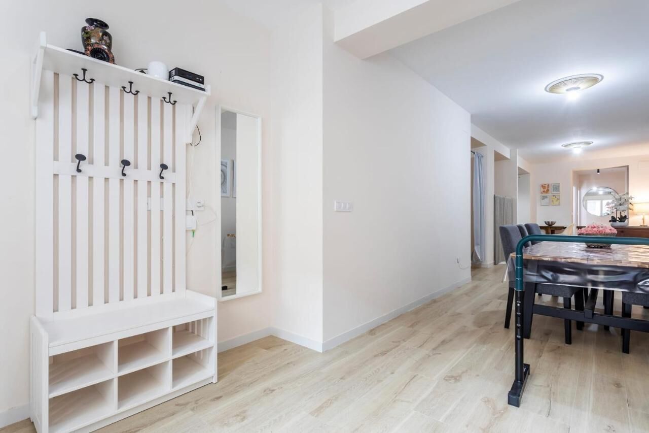 A hallway with a white coat rack, a dining area with a table and chairs, and a mirror on the wall.
