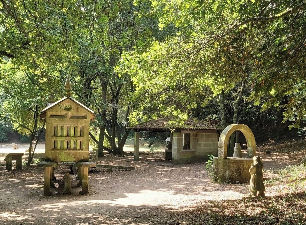 Ein rustikales Steinhaus mit kleinem Anbau, umgeben von Bäumen in einem bewaldeten Gebiet.