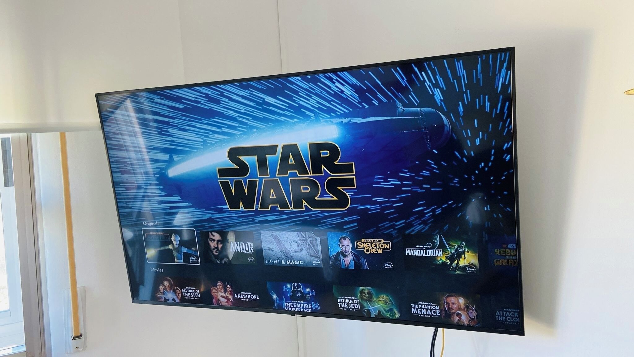 Ein an der Wand montierter Fernseher zeigt das Star Wars Logo und eine Auswahl an Star Wars Filmen.