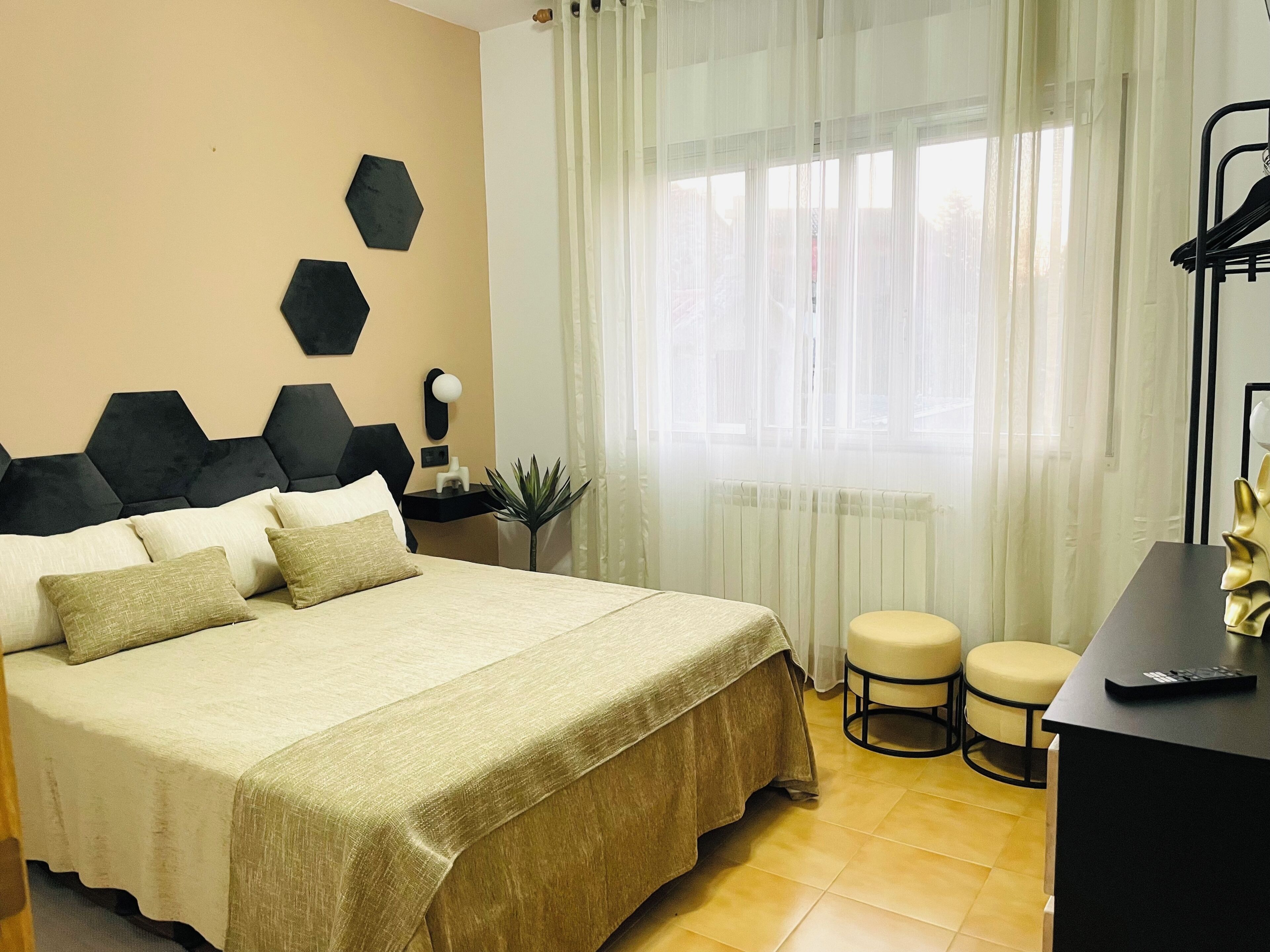 Habitación de hotel con cama, escritorio, silla y ventana con cortinas translúcidas.