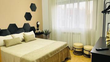 Habitación de hotel con cama, escritorio, silla y ventana con cortinas translúcidas.
