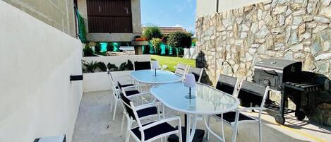 Un patio al aire libre con mesas y sillas redondas, un muro de piedra y una parrilla.
