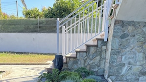 Un área de jardín ajardinada con un muro de piedra, una cerca de metal y una escalera que lleva a un edificio.