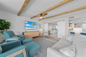 Un salon moderne avec des canapés bleu sarcelle et gris, un téléviseur à écran plat et un ventilateur de plafond.