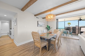 Un coin repas avec une table et des chaises en bois, un luminaire suspendu et une vue sur le balcon.