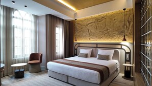A modern hotel room with a large bed, a seating area with a chair and table, and a textured wall feature. - Rempart Hotel (Diyarbakir)