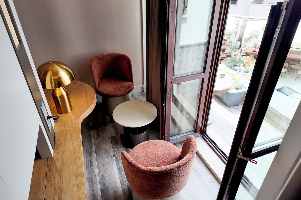 A corner of a room with a wooden floor, a round table, two red chairs, and a gold lamp.
