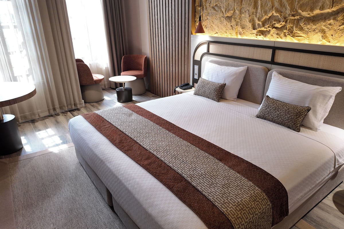 A modern hotel room with a large bed, a round side table, a chair, and a small round table.