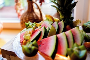 Een houten tafel met een fruitschaal, onder andere met watermeloen, kiwi en ananas.
