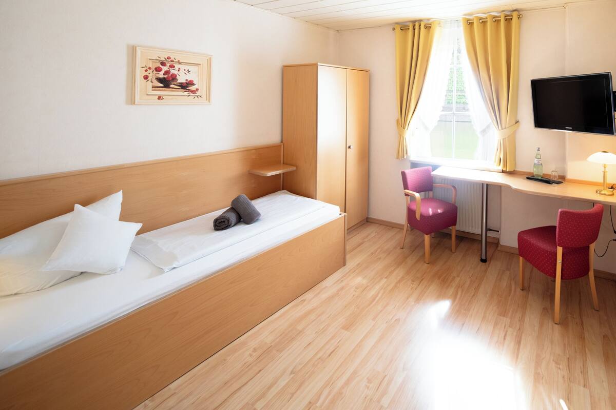 Een kamer met een bed, bureau, stoel, televisie en kledingkast.