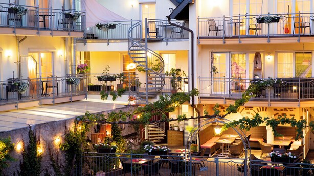 Un hotel de varios pisos con terraza al aire libre, una escalera en espiral y balcones con plantas.