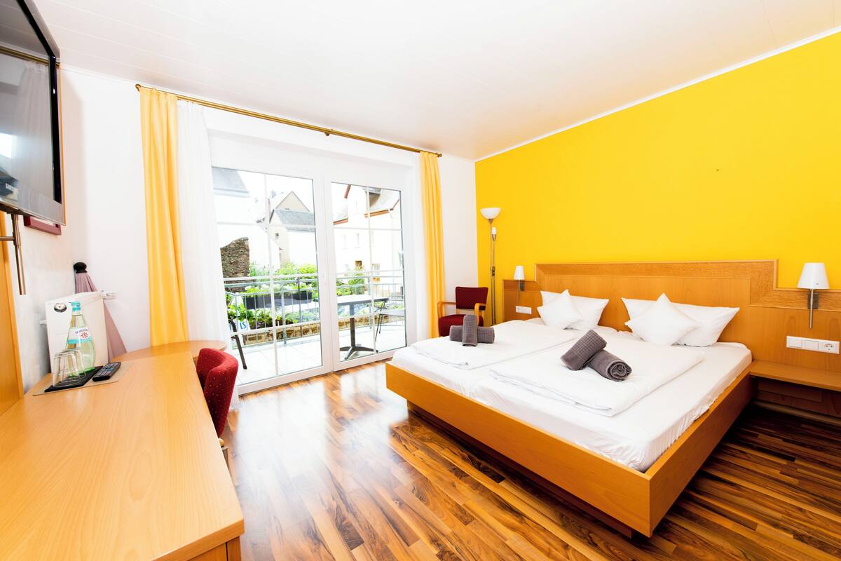 Een hotelkamer met een bed, een bureau, een stoel en een balkon met uitzicht.