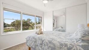 Un dormitorio con un ventanal grande, una cama con ropa de cama floral, un ventilador de techo y un espejo.