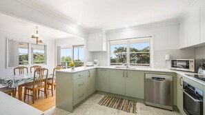 A modern kitchen with a dining area, large windows, and a view of greenery.