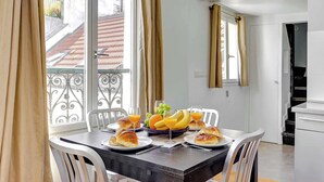 A dining area with a table set for breakfast, including croissants, fruit, and orange juice. - Cozy 1BR Near Champs-Élysées - Sleeps 4 (Paris)