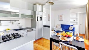 A modern kitchen with a gas stove, sink, and white cabinets. A dining area with a table set for breakfast, including croissants and fruit, is visible. - Cozy 1BR Near Champs-Élysées - Sleeps 4 (Paris)
