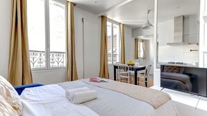 A hotel room with a bed, a desk, a chair, a television, and a balcony with curtains. - Cozy 1BR Near Champs-Élysées - Sleeps 4 (Paris)