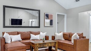 A living room with a brown leather sofa, a wooden coffee table, and a large mirror on the wall. - Checkmate and Chill-Inn I Yard Games, Families (Elgin)