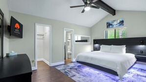 A bedroom with a bed, a ceiling fan, a nightstand, a desk, and a window with blinds. - Checkmate and Chill-Inn I Yard Games, Families (Elgin)