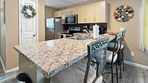 A kitchen with granite countertops, wooden cabinets, a refrigerator, a microwave, a sink, and a dining area with chairs. - No stairs, walk to marina, secluded, mins to strip (Branson)