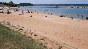 Ein Strand mit badenden und sonnenden Personen, bewölkter Himmel und Bäumen in der Ferne.