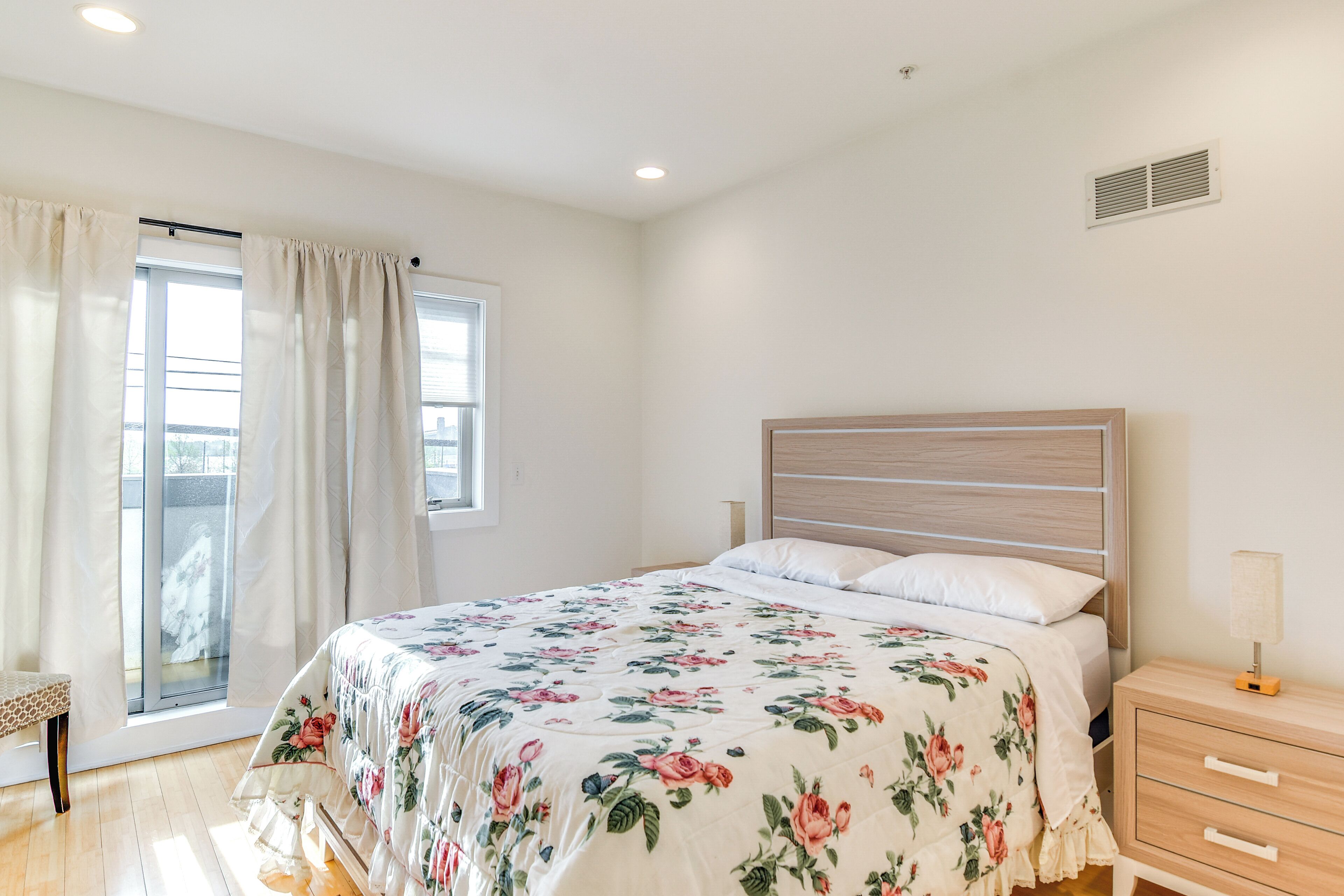 A bedroom with a bed, a nightstand, a bench, and a window with curtains.