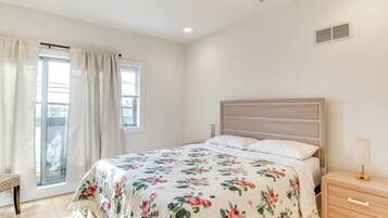 A bedroom with a bed, a nightstand, a bench, and a window with curtains.