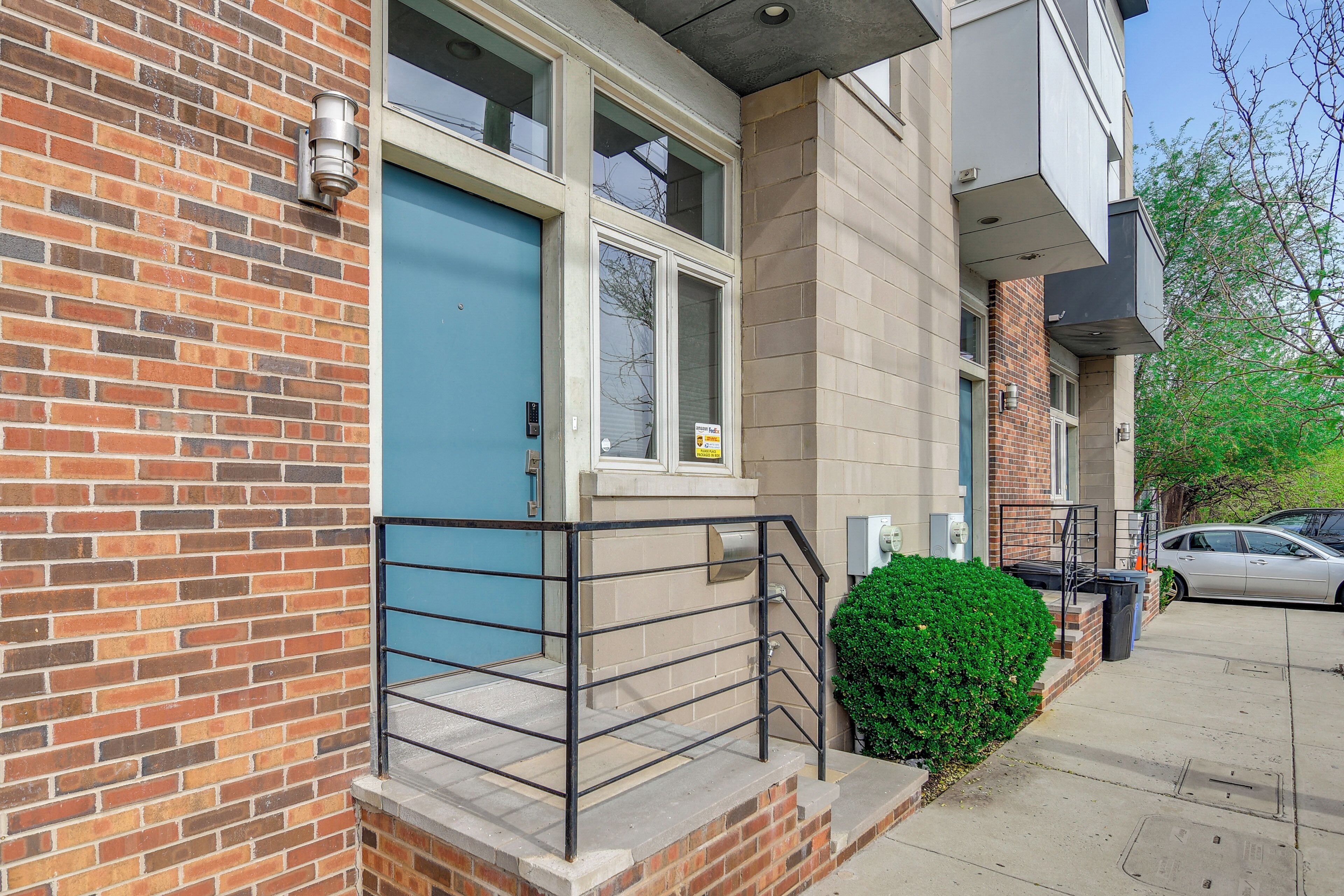 A residential building with a blue door, brick facade, and a small balcony with a metal railing.