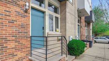 A residential building with a blue door, brick facade, and a small balcony with a metal railing.