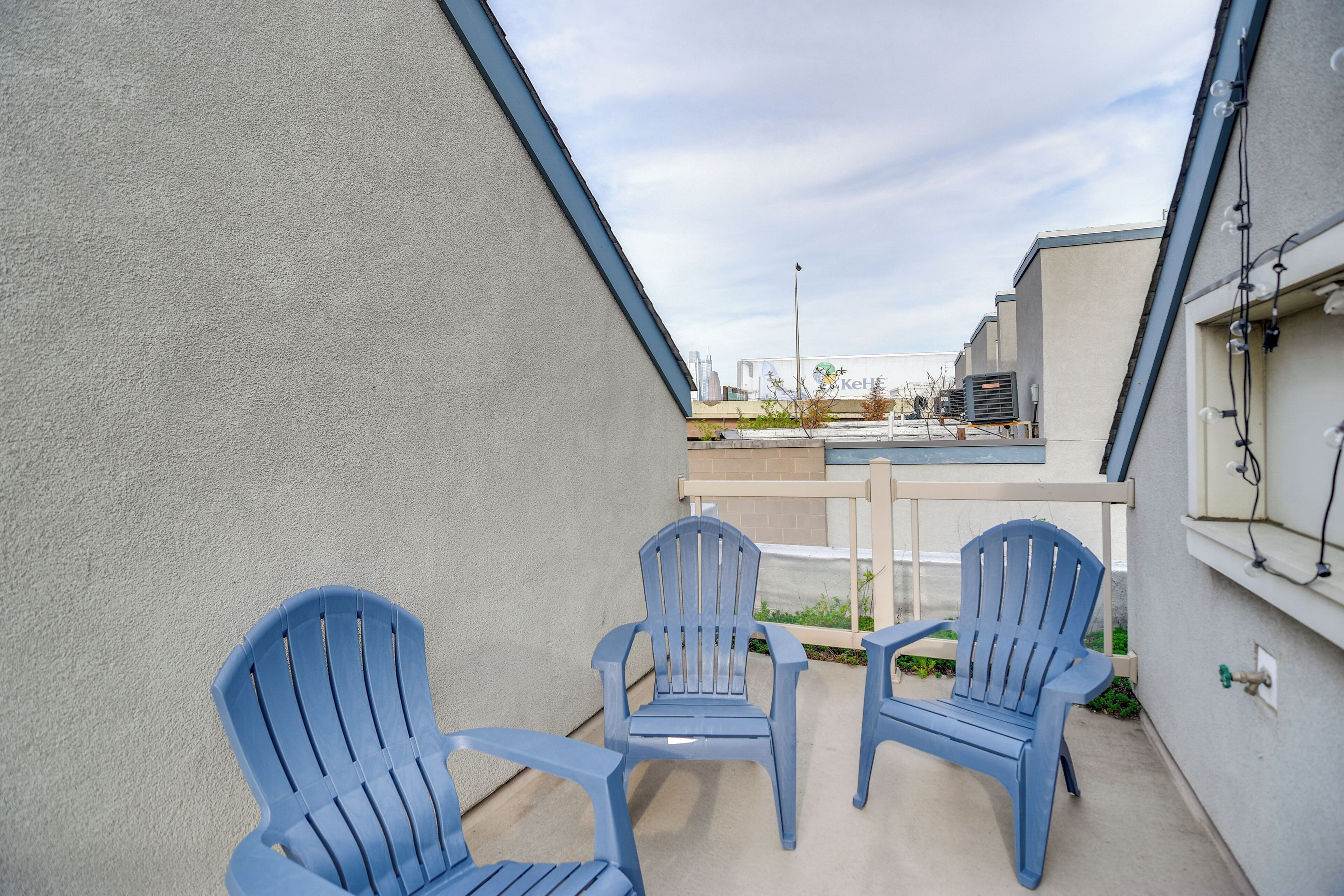 Un patio con dos sillas Adirondack azules, suelo de hormigón y vista a edificios al fondo.