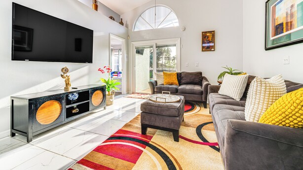 Een moderne woonkamer met een flatscreen televisie, een grijze bank, een kamerkleed met dessin en een console met decoratieve objecten.