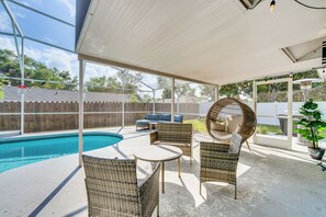 Un espacio al aire libre cubierto con piscina, mobiliario de mimbre y una zona de estar con una silla colgante.